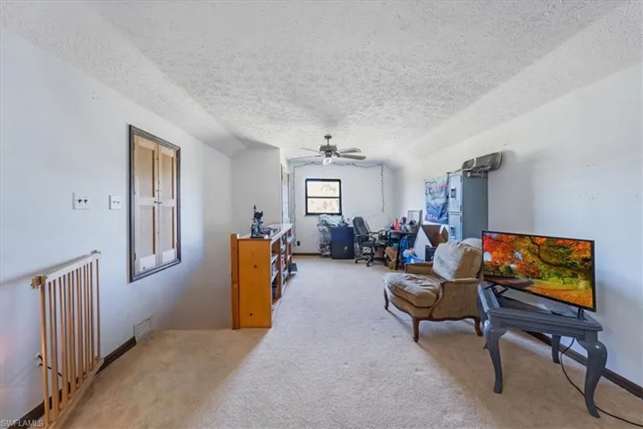 Living area with vaulted ceiling, ceiling fan, carpet floors, and a textured ceiling