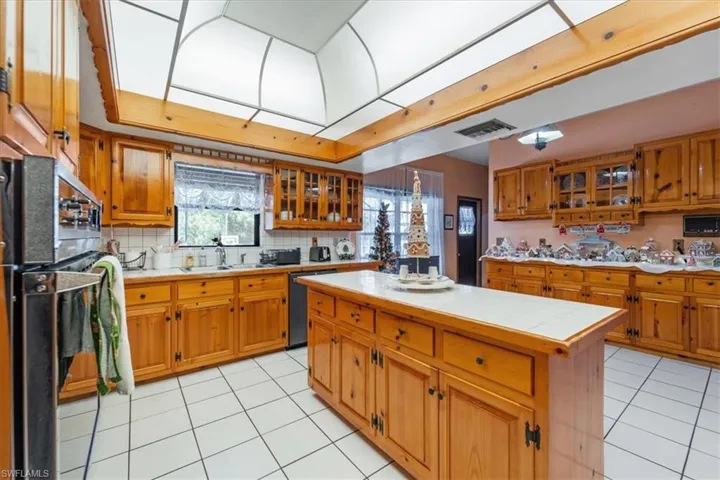 Kitchen featuring tile counters, dishwasher, light tile patterned floors, decorative backsplash, and a kitchen island