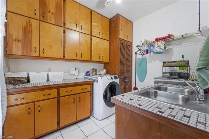 Clothes washing area featuring cabinets, washer / dryer, light tile patterned floors, and sink