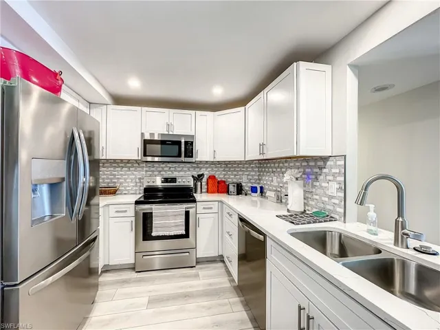 Kitchen featuring stainless steel appliances, white cabinetry, light stone counters, tasteful backsplash, and light wood-type flooring