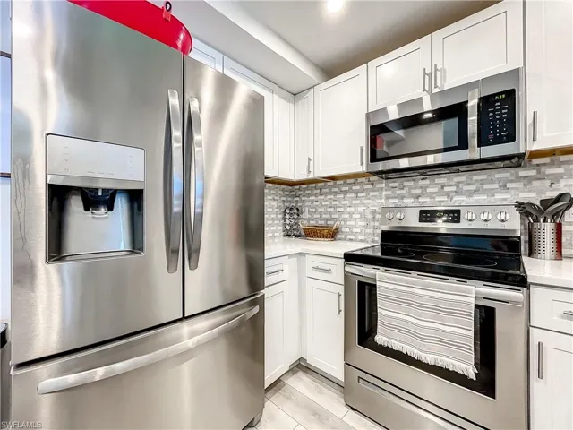 Kitchen with stainless steel appliances, white cabinetry, tasteful backsplash, light stone countertops, and light wood finished floors