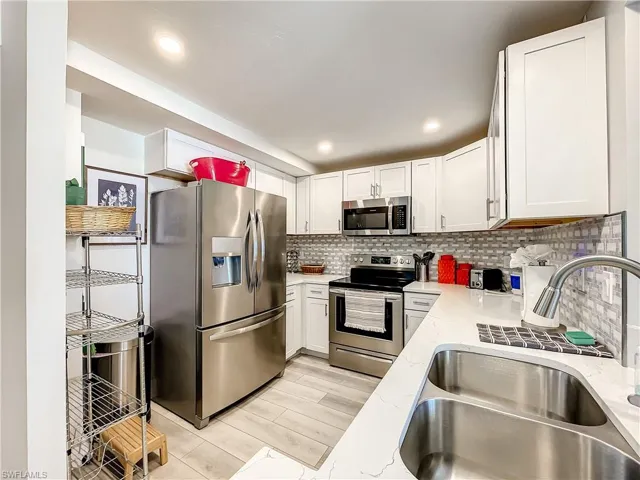 Kitchen with stainless steel appliances, white cabinetry, light stone countertops, tasteful backsplash, and wood finish floors