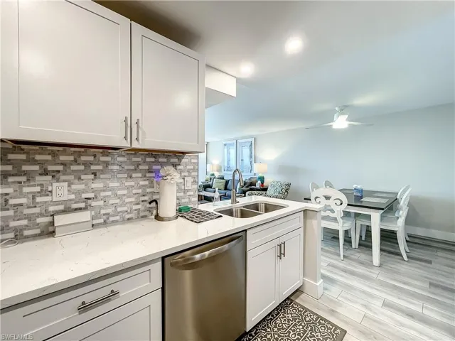 Kitchen featuring dishwasher, light stone counters, wood finish floors, white cabinets, and recessed lighting
