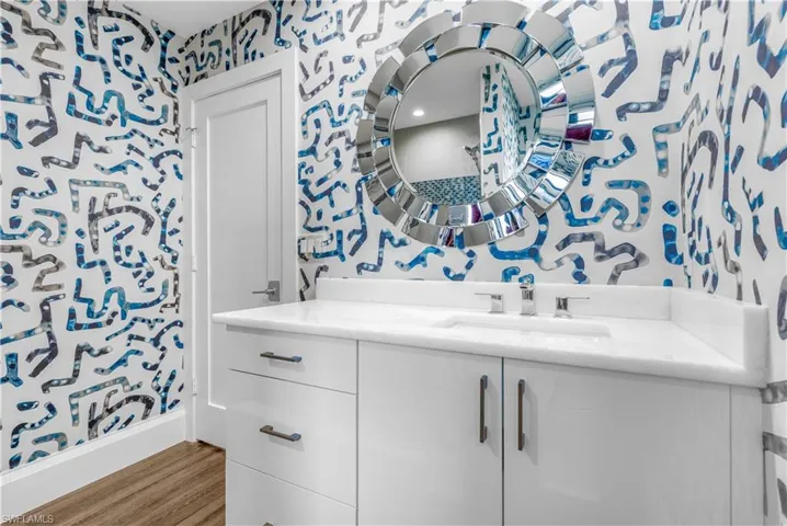 Bathroom vanity featuring a white countertop with an integrated sink, polished chrome faucet, and a decorative circular mirror