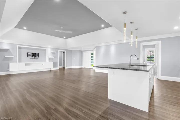 Spacious open-concept living area featuring wood-finish flooring, a built-in entertainment center, a central island with a sink and dark countertop, recessed lighting, and modern pendant fixtures