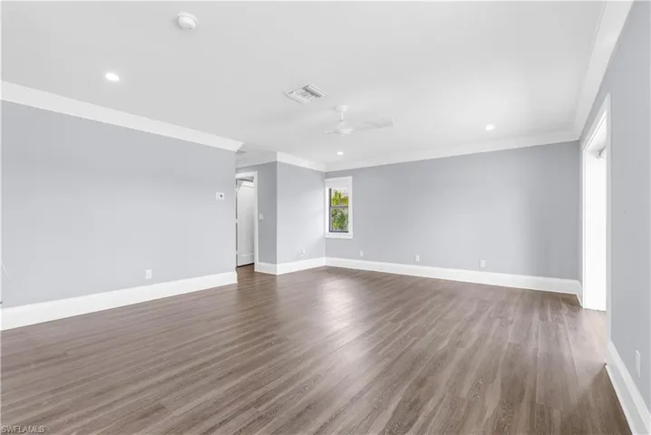 Spacious room featuring wood-finish flooring, light blue walls, white crown molding, recessed lighting, and a ceiling fan