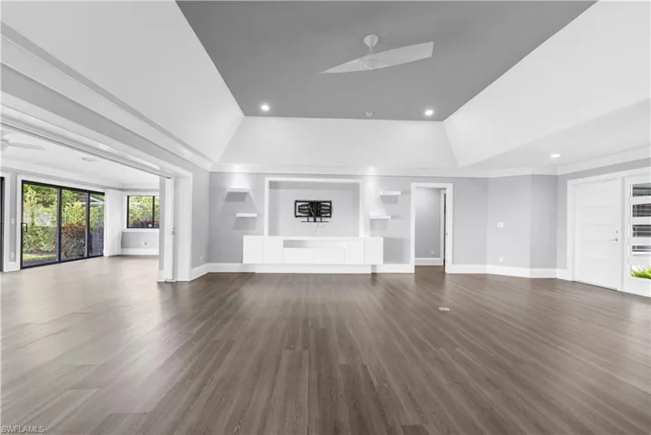 Expansive room featuring wood-finish flooring, a tray ceiling with recessed lighting and a ceiling fan, and a built-in media console with floating shelves