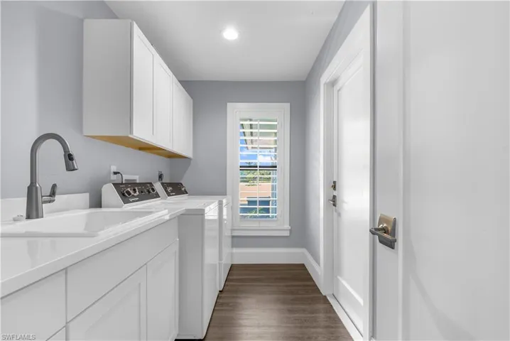 Dedicated laundry room featuring white cabinetry with under-cabinet wood trim, a built-in sink with a matte gray faucet, and wood-finish flooring