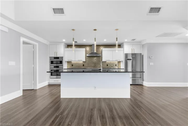 Contemporary kitchen featuring a central island with a dark countertop, stainless steel appliances, white cabinetry, a tiled backsplash, and wood-finish flooring