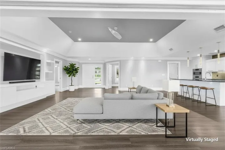 Spacious open-concept interior featuring wood-finish flooring, a contemporary kitchen island with seating, a built-in media console, recessed lighting, and a tray ceiling