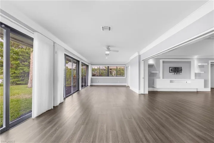 Spacious interior featuring wood-finish flooring, extensive sliding glass doors, and a built-in media center with shelving