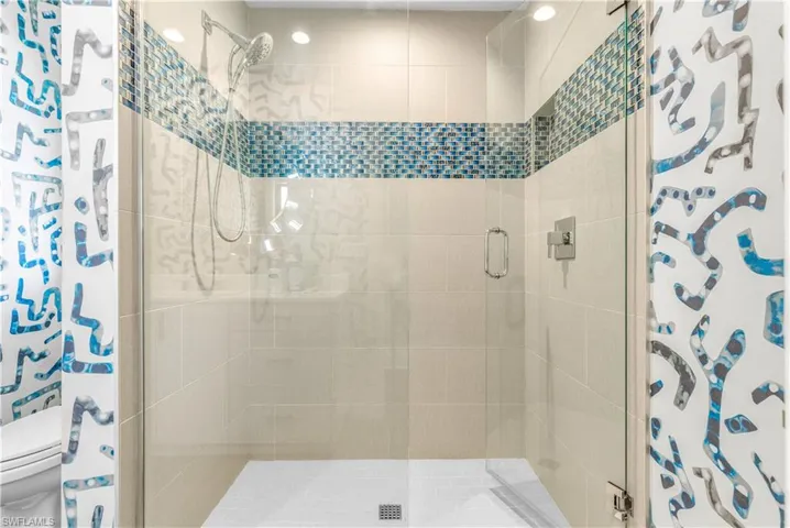 Glass-enclosed shower with a contemporary handheld shower fixture, accent mosaic tile band, recessed lighting, and a neutral-toned tile surround