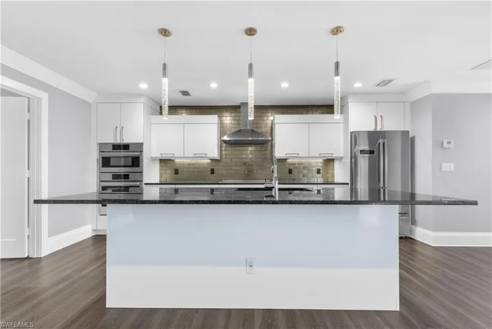 Kitchen featuring a large island with dark countertop, white cabinetry, stainless steel appliances, and wood-finish flooring