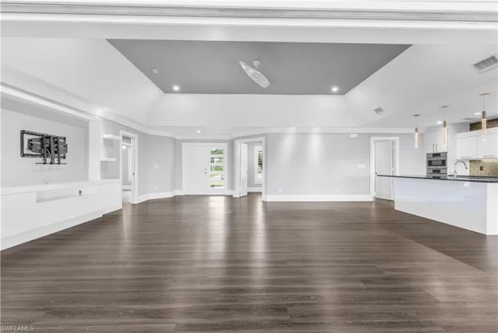 Spacious interior featuring wide plank wood-finish flooring, a recessed ceiling with a contemporary ceiling fan, and built-in cabinetry with shelving