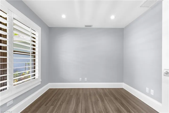 Room featuring wood-finish flooring, light grey painted walls, white trim, and a window with plantation shutters