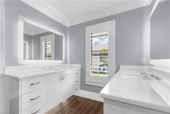 Bathroom vanity with wood-finish flooring, white cabinetry, integrated sinks, chrome hardware, and a large framed mirror