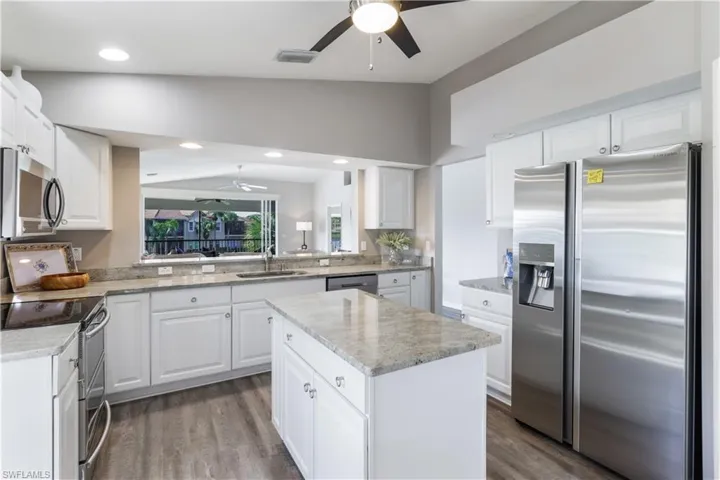 Kitchen featuring lofted ceiling, white cabinets, hardwood / wood-style floors, stainless steel appliances, and a center island