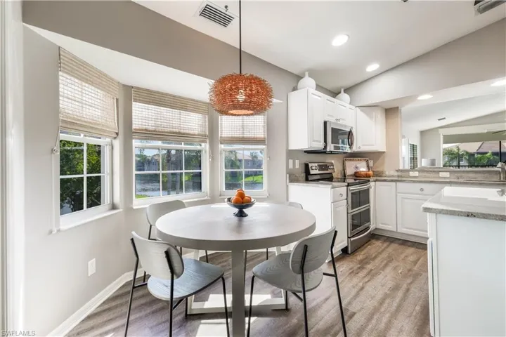 Kitchen featuring lofted ceiling, decorative light fixtures, white cabinets, and stainless steel appliances