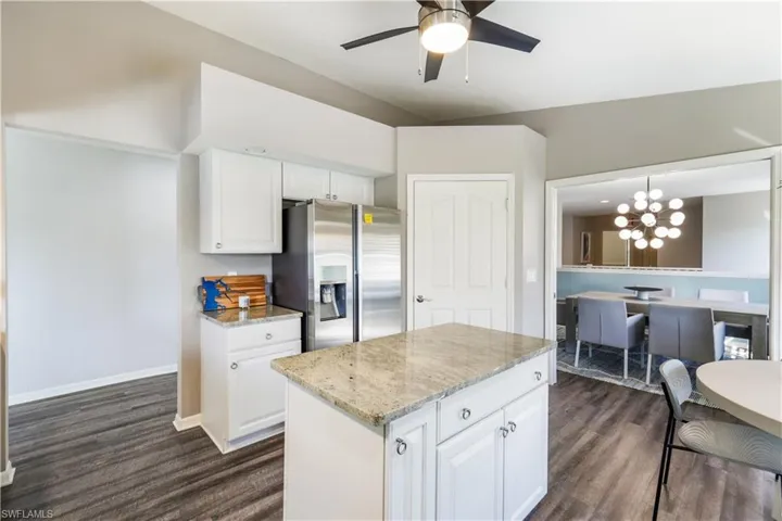 Kitchen with stainless steel fridge, white cabinets, decorative light fixtures, and dark hardwood / wood-style floors