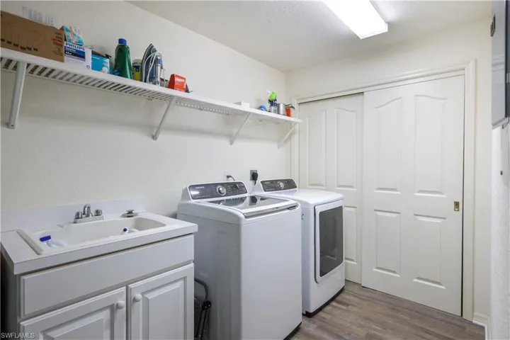 Laundry area with cabinets, a textured ceiling, hardwood / wood-style flooring, sink, and washer and clothes dryer