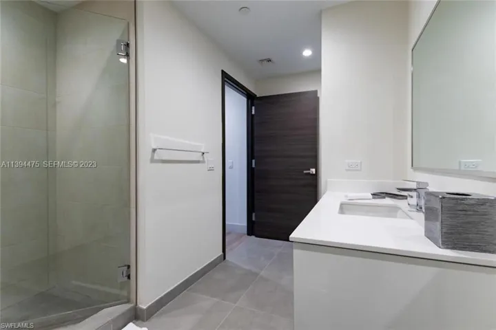 Bathroom featuring a frameless glass shower enclosure, a single vanity with an integrated sink and white countertop, and contemporary gray tile flooring