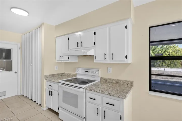 Kitchen featuring white electric stove, white cabinetry, light tile patterned flooring, and light stone counters