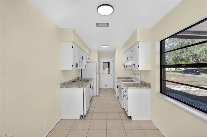 Kitchen featuring white appliances, light countertops, light tile patterned flooring, and white cabinetry