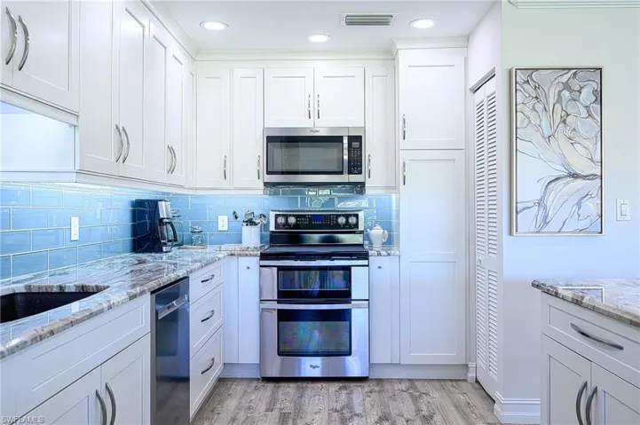 Kitchen featuring white cabinets, light wood-type flooring, tasteful backsplash, light stone counters, and stainless steel appliances