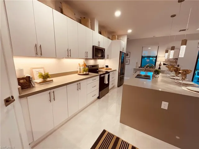 Kitchen with sink, white cabinetry, hanging light fixtures, appliances with stainless steel finishes, and light tile patterned floors