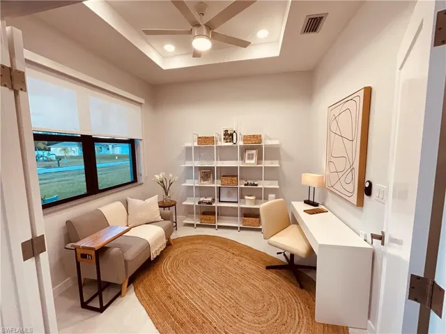 Living area with ceiling fan, a raised ceiling, and light tile patterned floors