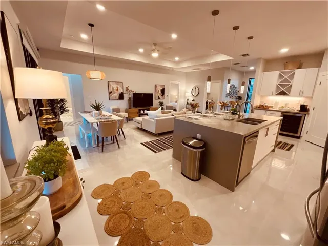 Kitchen featuring a center island with sink, stainless steel dishwasher, a tray ceiling, and white cabinets
