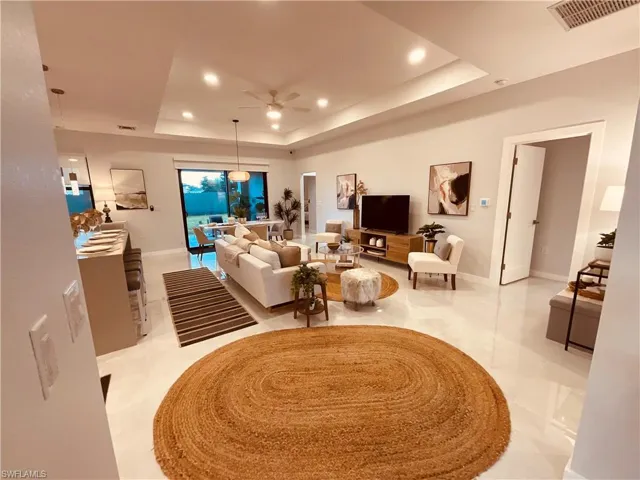 Living room featuring a tray ceiling, ceiling fan, and light tile patterned floors