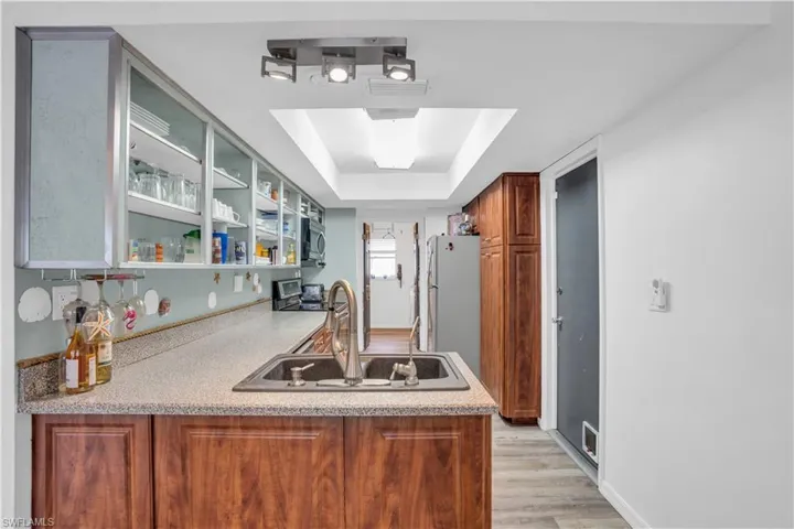Kitchen with glass insert cabinets, a tray ceiling, light countertops, and a sink