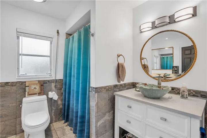 Bathroom with wainscoting, tile walls, toilet, and vanity