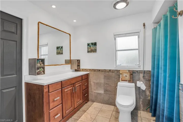 Full bath with toilet, recessed lighting, a wainscoted wall, vanity, and tile walls