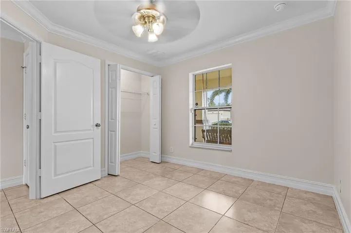 Unfurnished bedroom with a closet, light tile patterned floors, ceiling fan, and crown molding