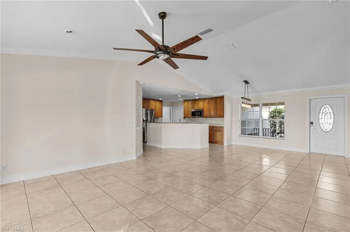 Unfurnished living room with ceiling fan, crown molding, light tile patterned floors, and vaulted ceiling