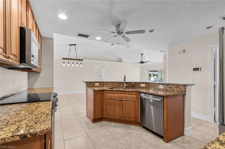 Kitchen featuring stainless steel appliances, decorative light fixtures, sink, an island with sink, and vaulted ceiling