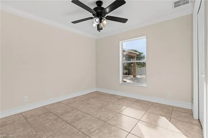 Tiled empty room featuring ceiling fan and crown molding