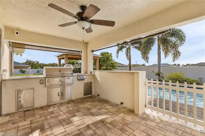 View of patio featuring exterior kitchen, ceiling fan, a fenced in pool, and grilling area