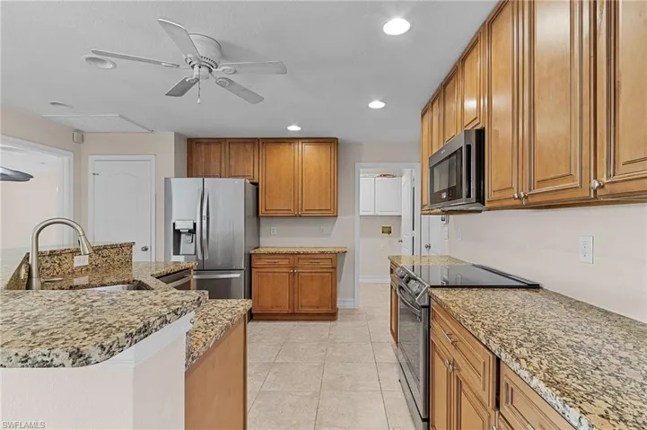 Kitchen with sink, ceiling fan, light tile patterned flooring, light stone countertops, and appliances with stainless steel finishes