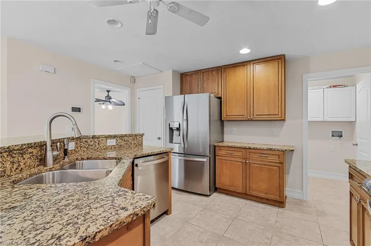 Kitchen featuring light tile patterned floors, sink, light stone counters, and appliances with stainless steel finishes