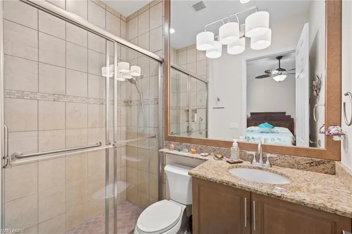 Bathroom featuring ceiling fan, vanity, walk in shower, and toilet
