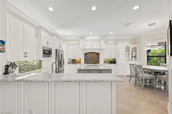 Kitchen featuring white cabinets, backsplash, kitchen peninsula, light tile patterned floors, and stainless steel appliances