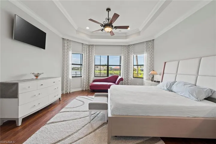 Bedroom with ornamental molding, a tray ceiling, ceiling fan, and dark wood-type flooring