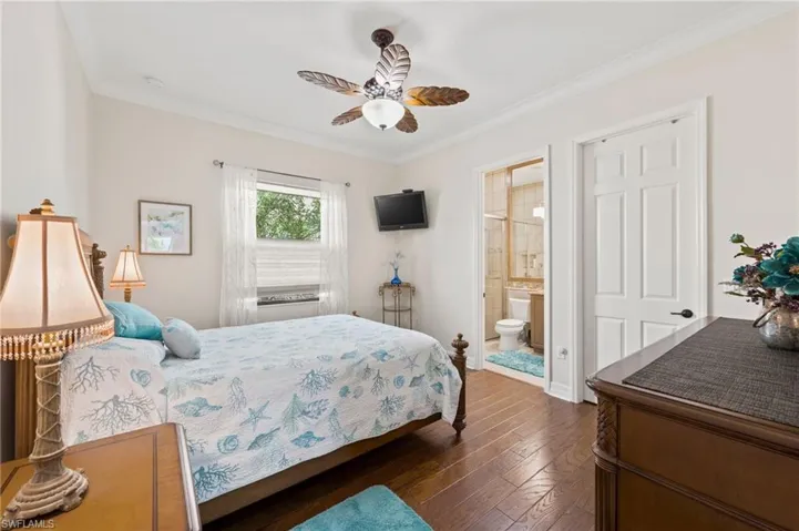 Bedroom with ensuite bath, ceiling fan, dark wood-type flooring, and crown molding