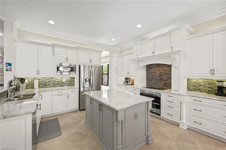 Kitchen with appliances with stainless steel finishes, white cabinets, tasteful backsplash, a center island, and sink
