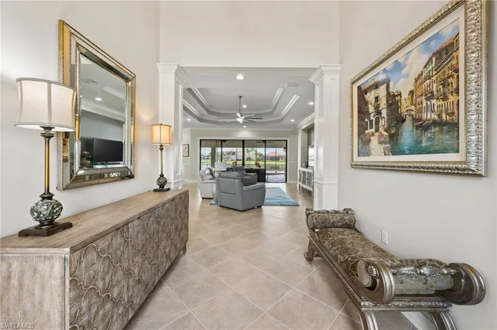 Hallway featuring ornate columns, a tray ceiling, crown molding, and light tile patterned floors