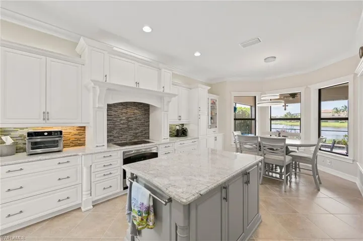 Kitchen with white cabinets, a kitchen island, light tile patterned floors, and tasteful backsplash