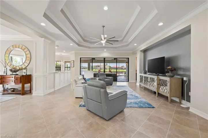 Living room featuring crown molding, light tile patterned flooring, a tray ceiling, and ceiling fan